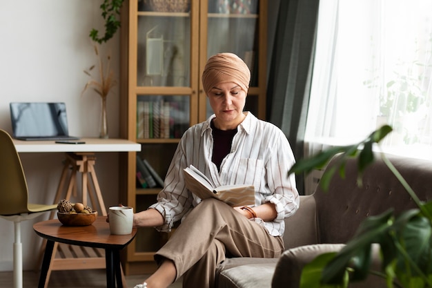 Imagem mulher em tratamento contra o câncer de mama lendo livro na sala de casa
