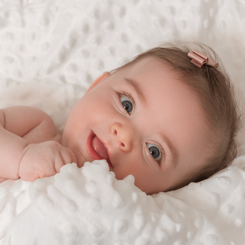 imagem de um bebê de olhos azuis sorrindo no meio do cobertor Laço Bebê Plush com Sherpa Dots Bolinhas