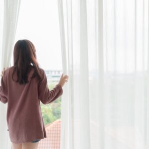 mulher na janela com a mão na cortina